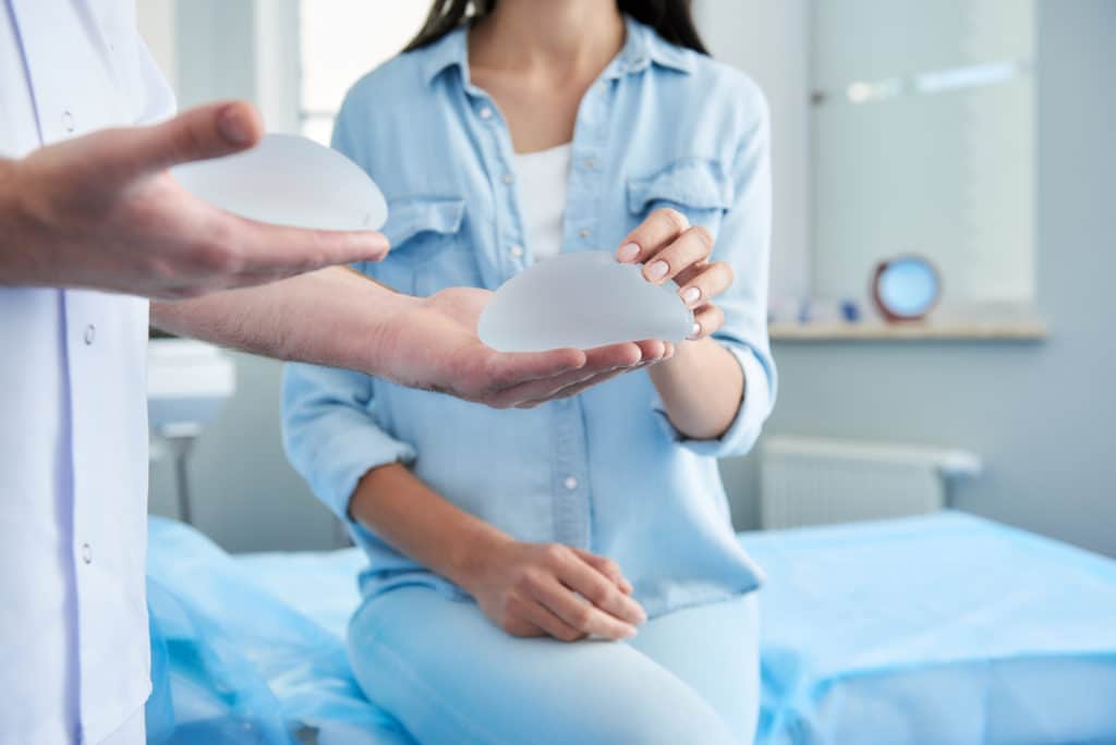Breast implants, doctor holding two implants with patient